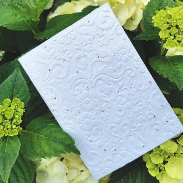 Weiße Seedgirls Karte aus Samenpapier mit handgeprägter Blütenranke vor blühender Hortensie